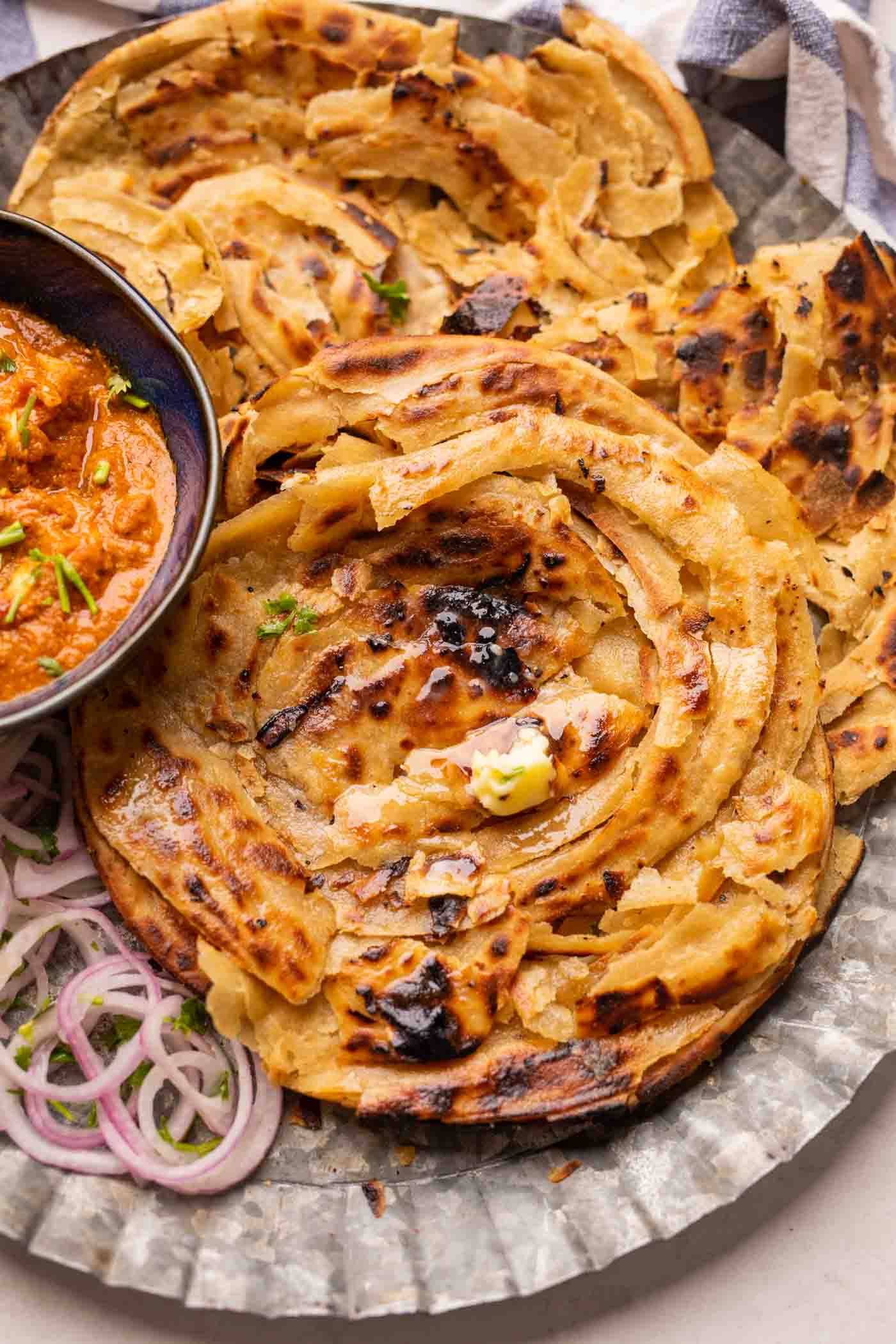 Lachha Parathas served on a plate with curry and onions
