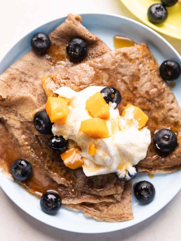 Ragi Crepes served on a plate topped with whipped cream, mango and blueberries