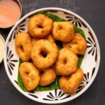 Medu vada served over a banana leaf in a bowl with chutney and sambar on the side