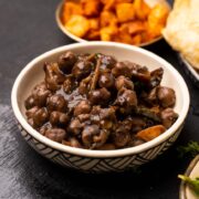 Bowl of pindi chole served with bhatura and potatoes on the side