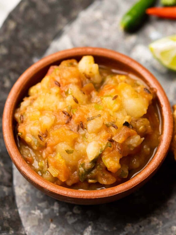 Picture of potato curry served in a brown terracotta bowl with puri on the side