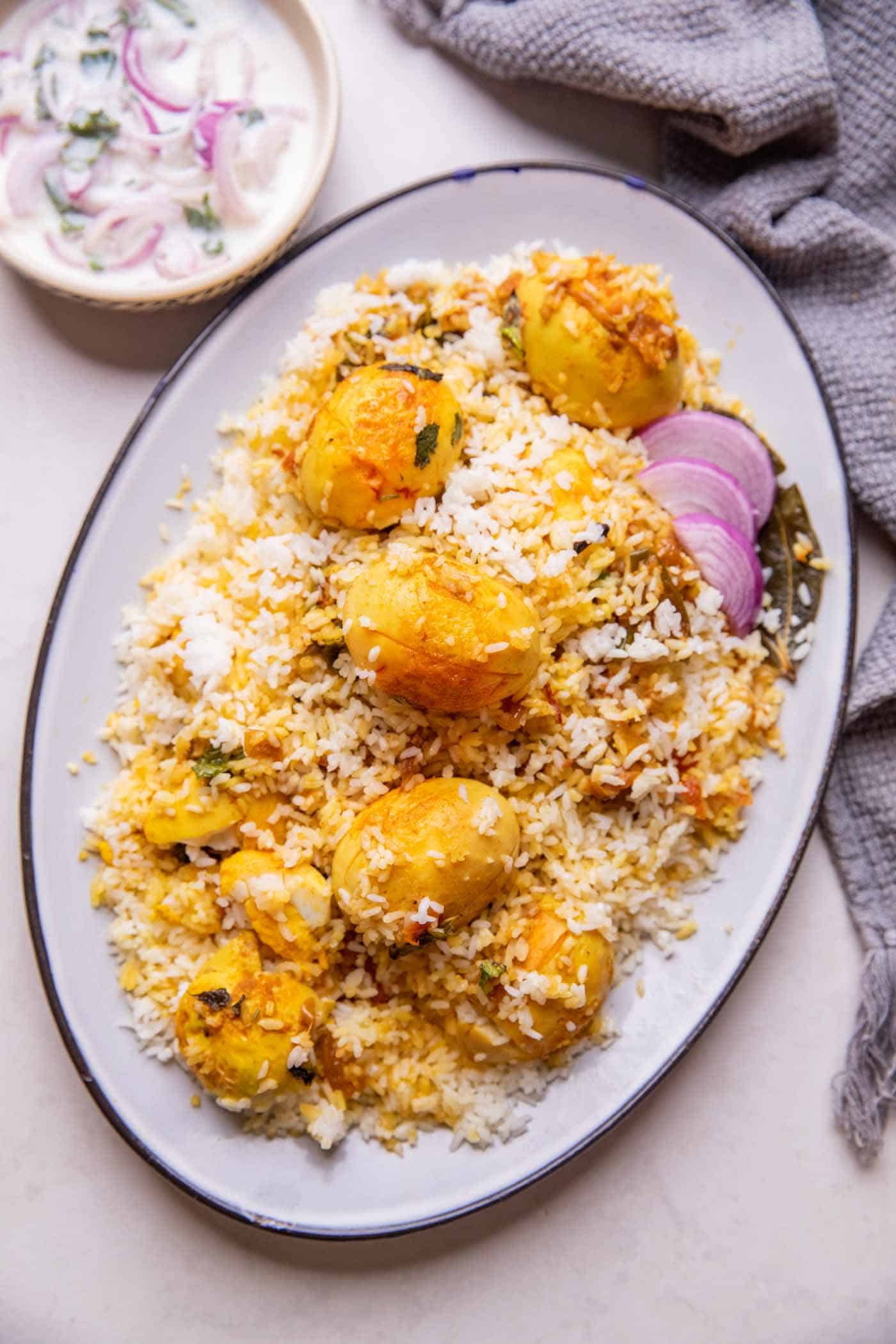 Egg Biryani served on a white platter with onion raita on the side