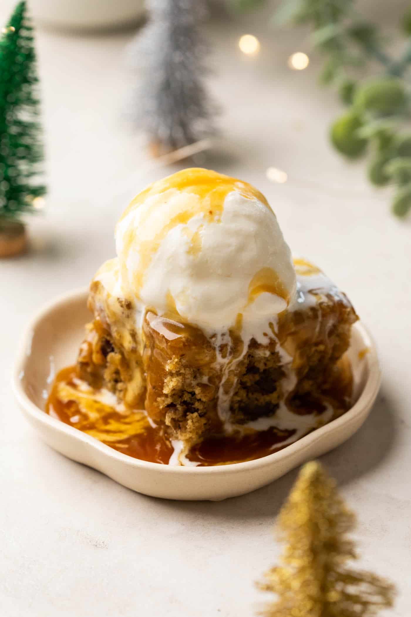 Sticky Toffee Pudding served on a white dessert plate topped with vanilla ice cream and toffee sauce