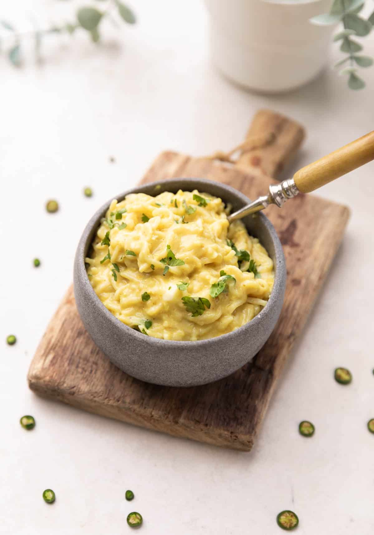 A shot of cheese and egg maggi in a grey bowl on a brown board