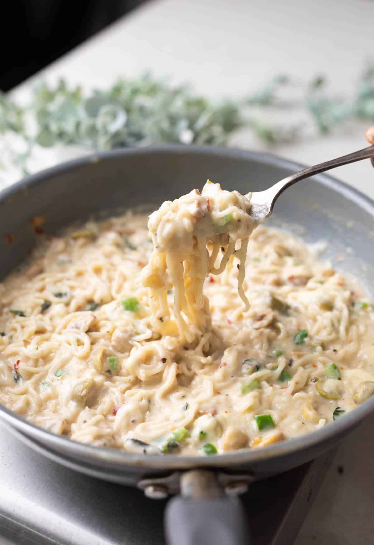 A shot of alfredo maggi in a grey pan with a fork full of noodles