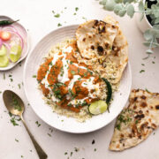 A plate of chicken tikka masala drizzled with cream served on top of rice along with a piece of naan