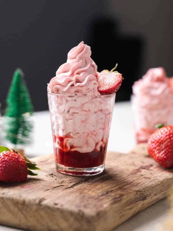 Strawberry mousse layered in a glass with strawberry compote topped with half a strawberry on a wooden board.