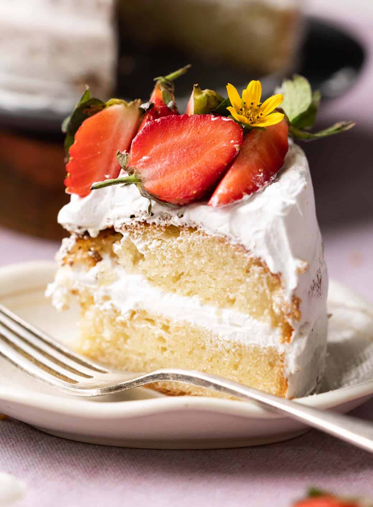 A slice of eggless vanilla cake layered with whipped cream and topped with strawberries