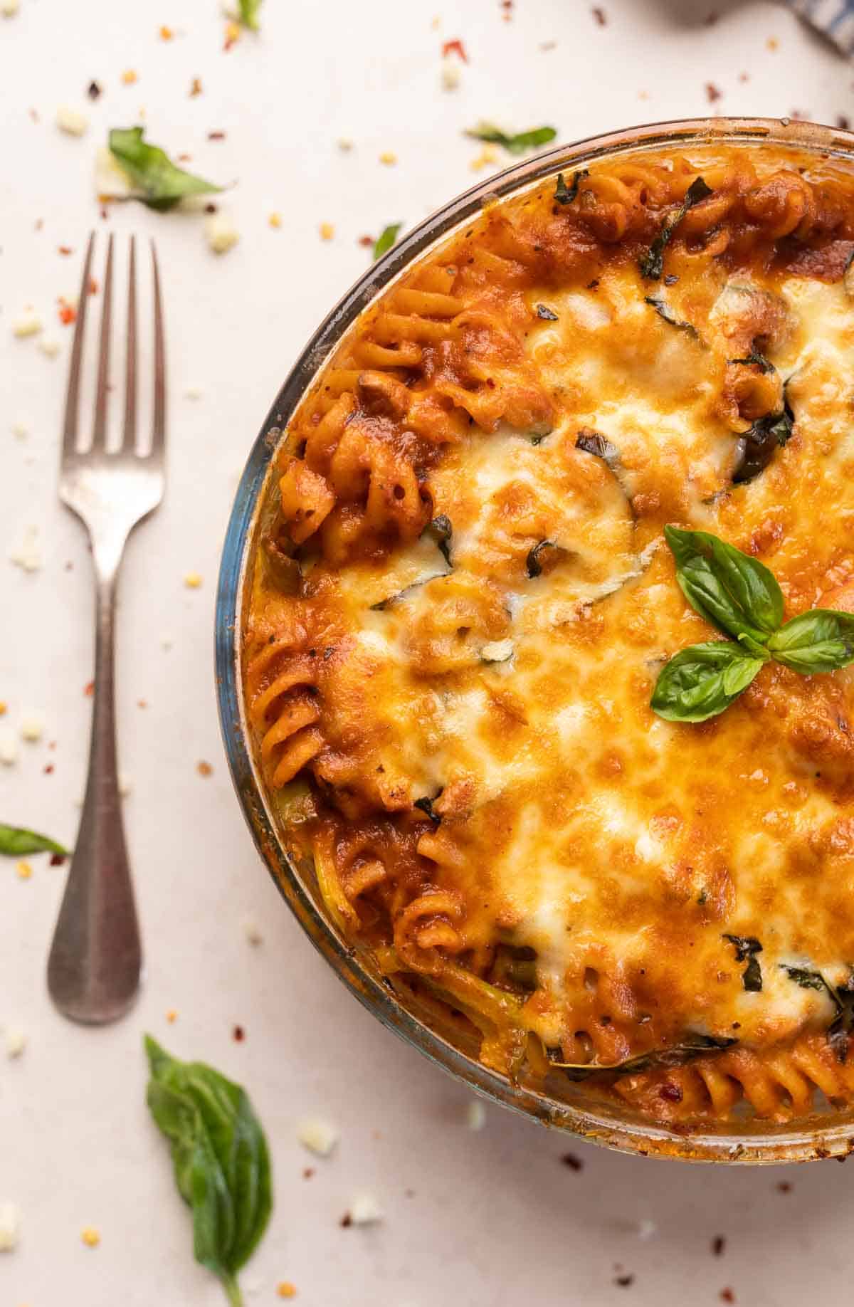 Red sauce pasta made in an air fryer served in a white bowl with melted cheese and basil on top