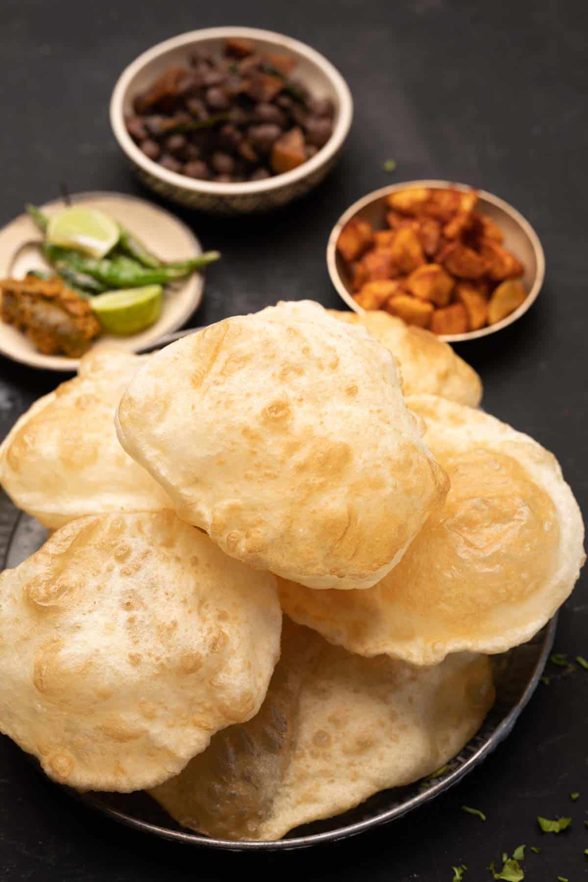a shot of puris in a plate with chole, fried aloos and chillies, lemon and pickle on the side
