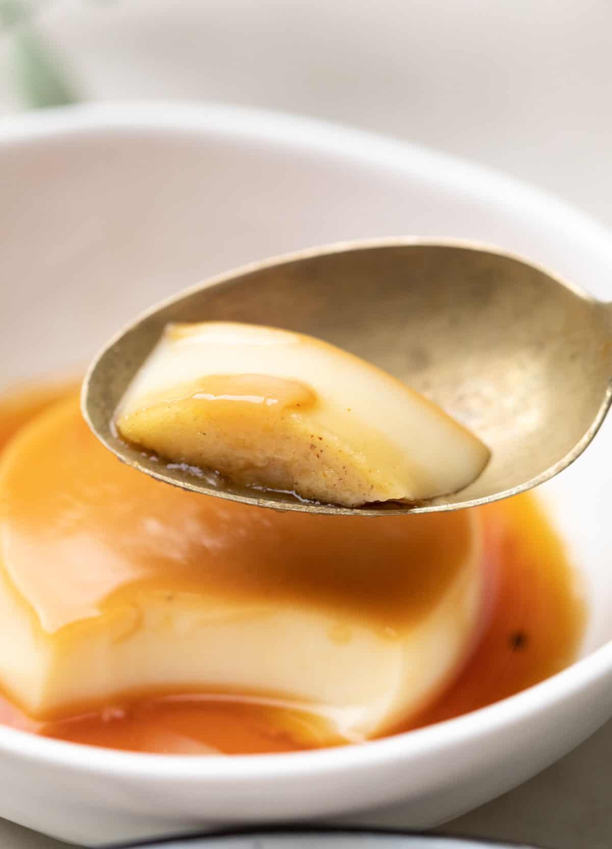 shot of a bite of caramel custard on a steel spoon