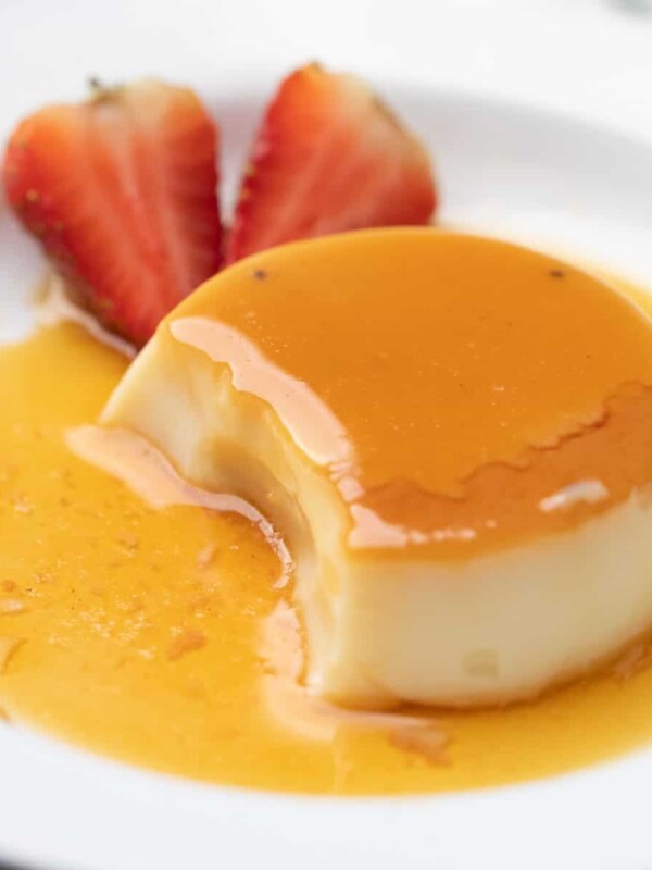 caramel cusstard served on a white plate with strawberries on the side.