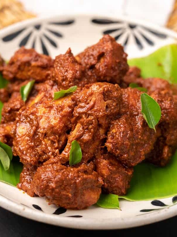 chicken ghee roast served on a white bowl over a plantain leaf