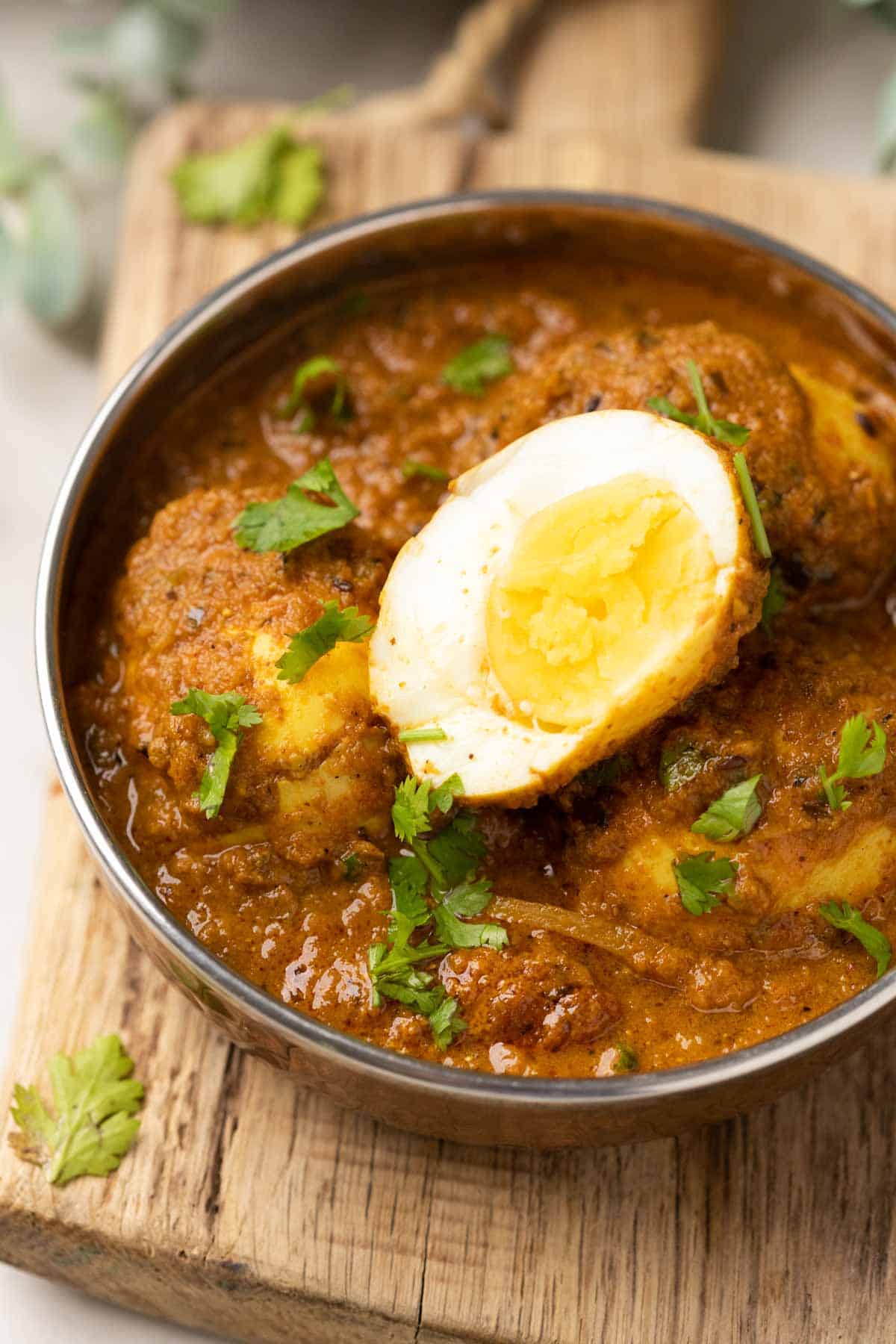 shot of egg curry in a steel bowl topped with coriander leaves