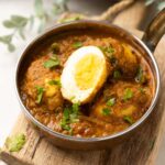 shot of egg curry in a steel bowl topped with coriander leaves