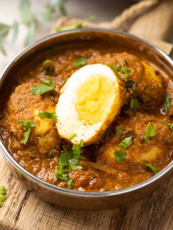 shot of egg curry in a steel bowl topped with coriander leaves
