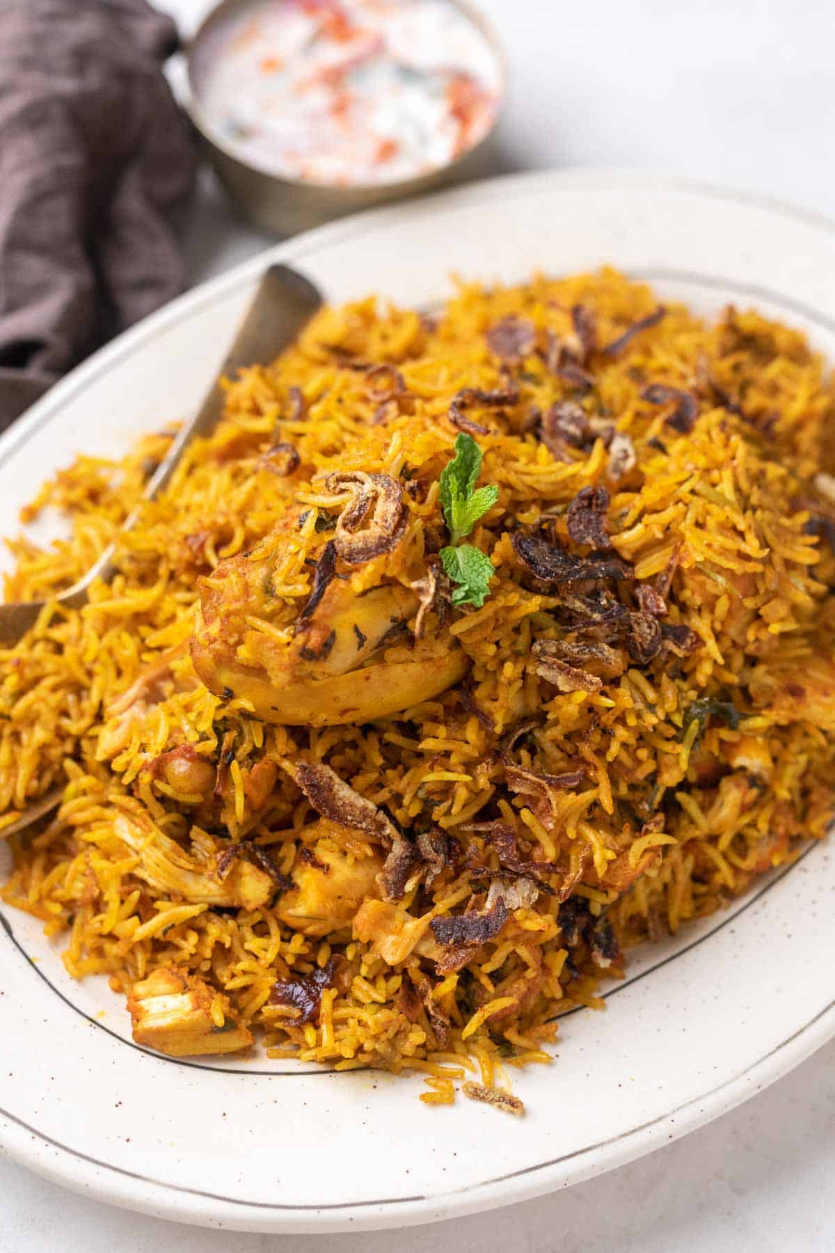 a white plate full of chicken biryani with raita on the side