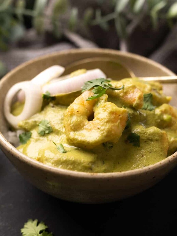 a bowl with white rice topped with green prawn curry with roundels of o