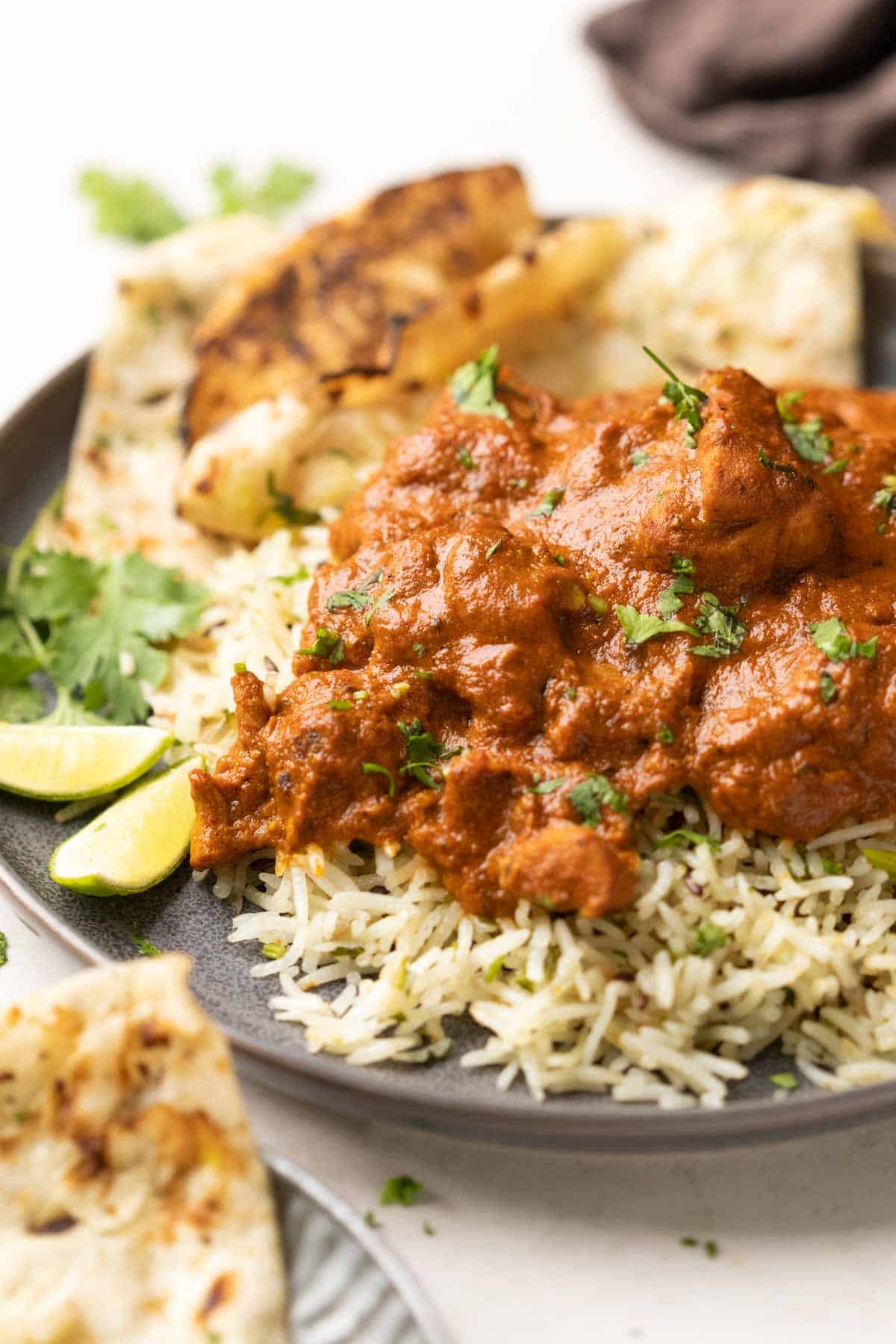 a plate of jeera rice topped with chicken tikka masala with a side of naan
