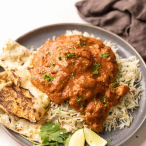 a plate of jeera rice topped with chicken tikka masala with a side of naan