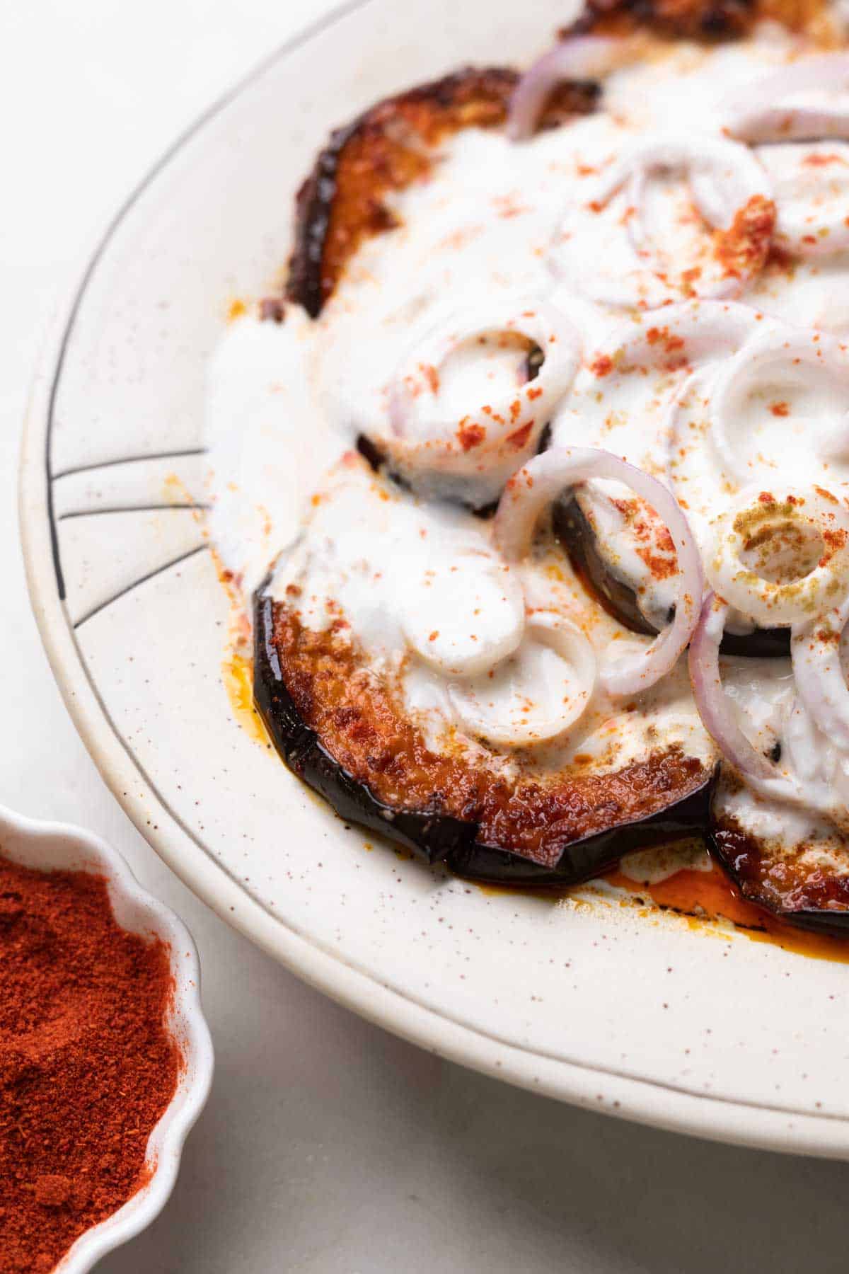 close up of platter with fried eggplant slices and sliced onion topped with a curd mix