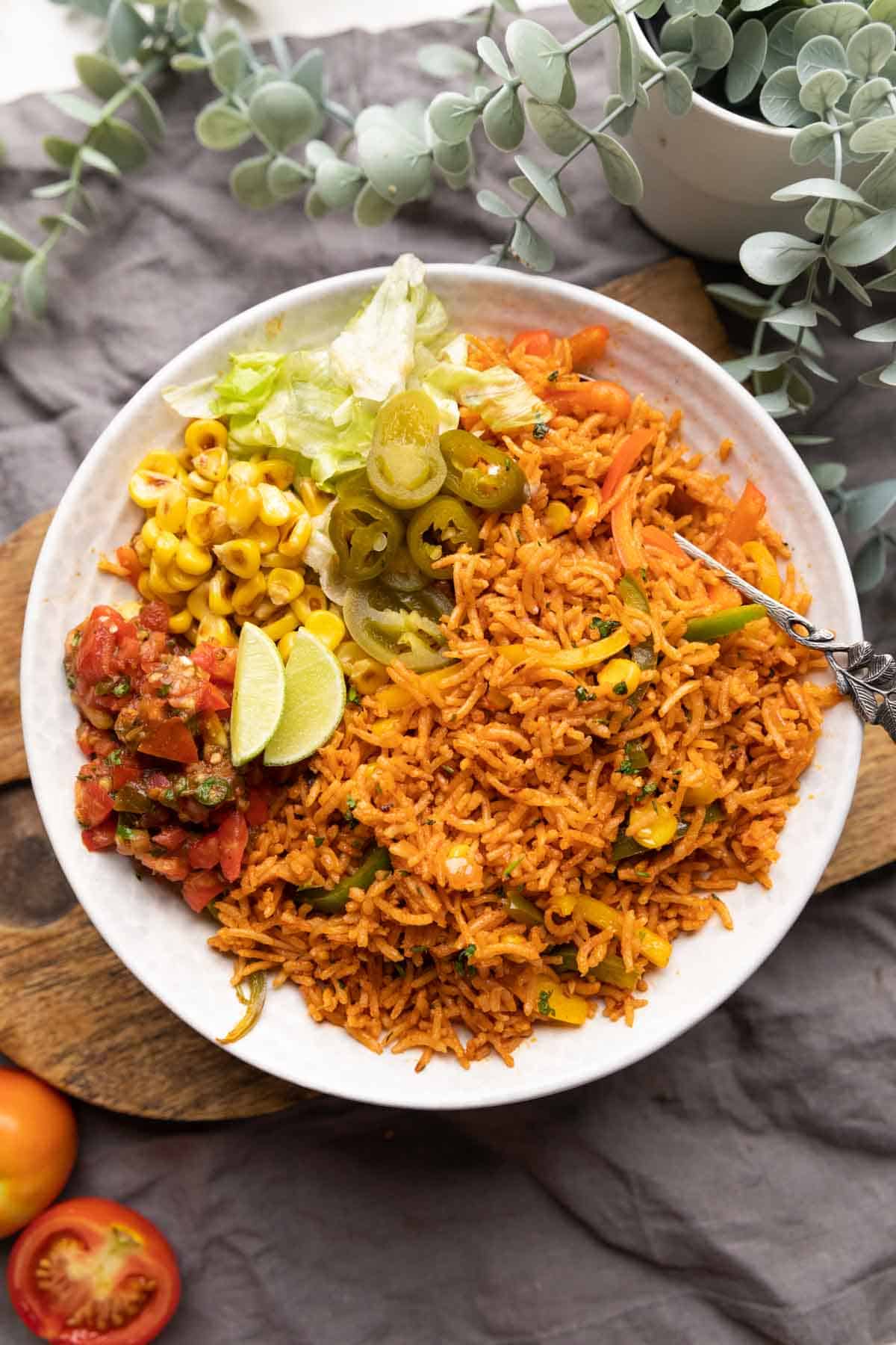 Instant Pot mexican rice served in a bowl with letttuce, corn, salsa, jalapenos and lime wedges on the side.