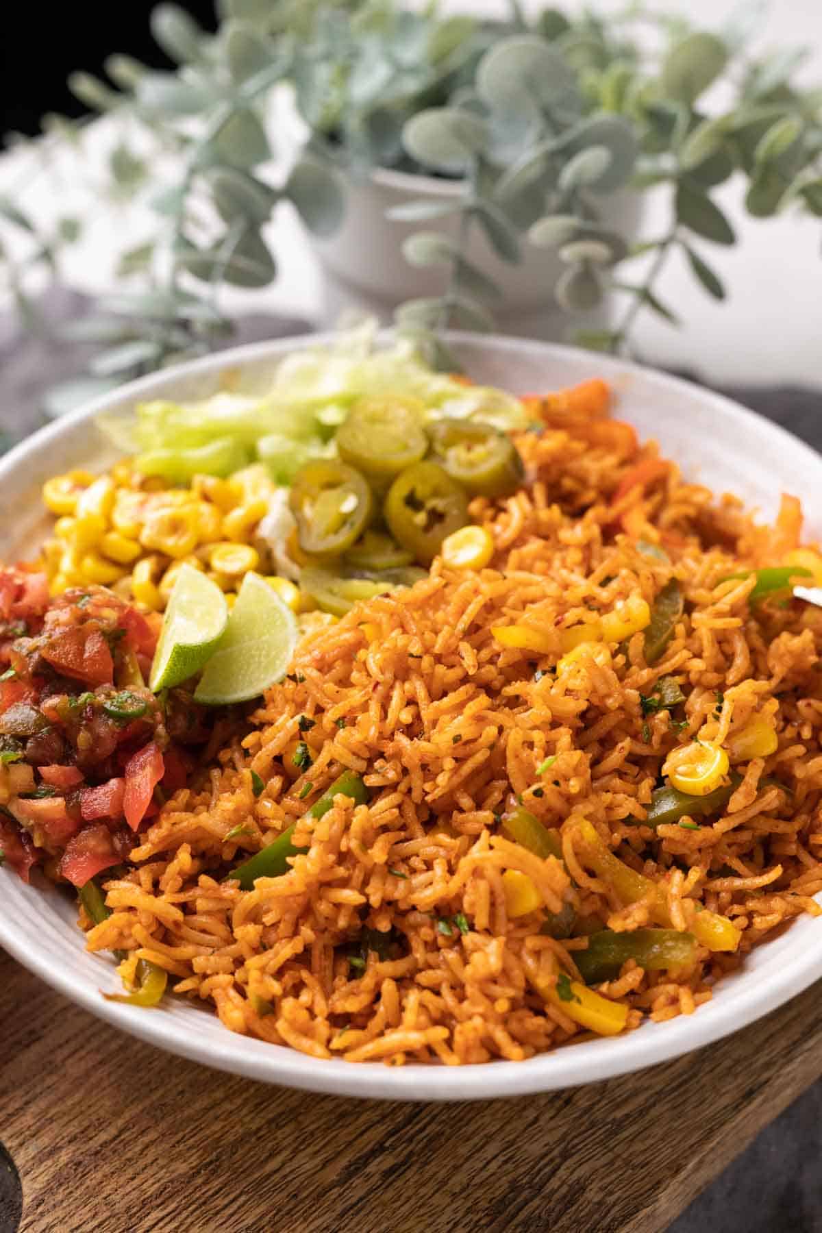 Instant Pot mexican rice served in a bowl with letttuce, corn, salsa, jalapenos and lime wedges on the side.