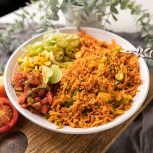 Instant Pot mexican rice served in a bowl with letttuce, corn, salsa, jalapenos and lime wedges on the side.