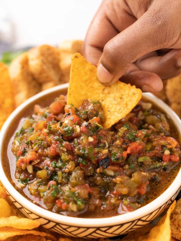 a nacho chip being dipped into a bowl of tomato salsa