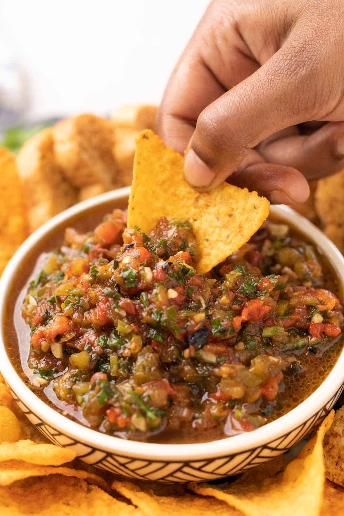 a nacho chip being dipped into a bowl of tomato salsa