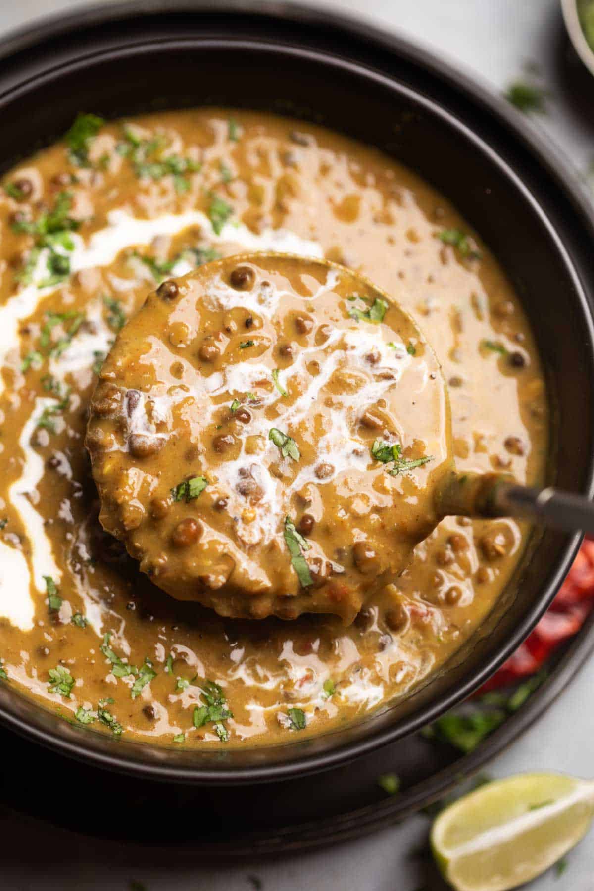 A ladleful of creamy amritsari dal coming out of a bowl