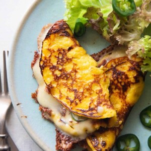 an image of cheese filled cachapa on a blue plate with sliced jalapeno and lettuce on the side