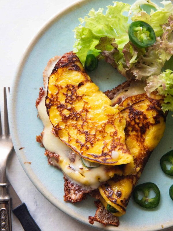 an image of cheese filled cachapa on a blue plate with sliced jalapeno and lettuce on the side
