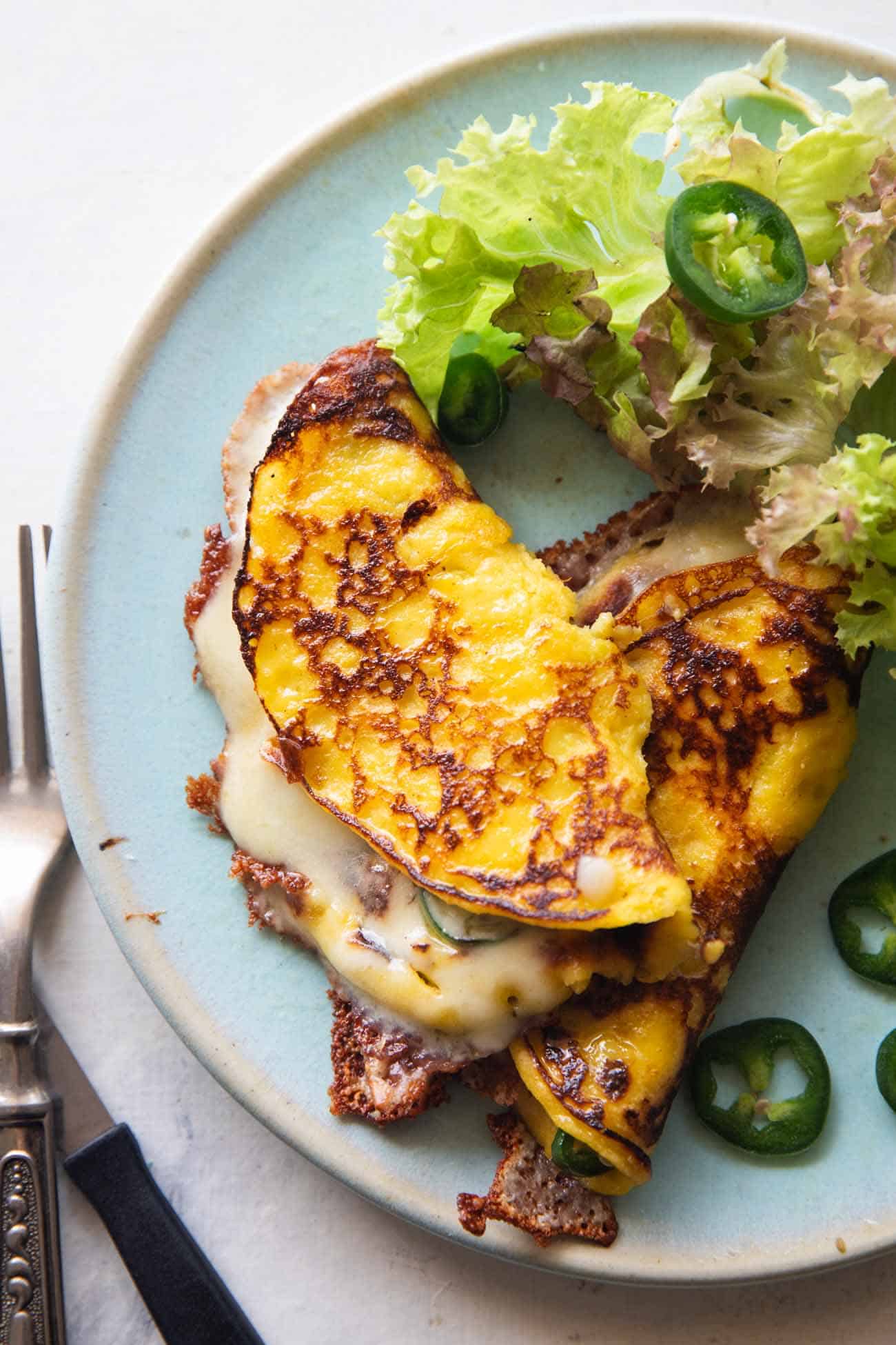 an image of cheese filled cachapa on a blue plate with sliced jalapeno and lettuce on the side
