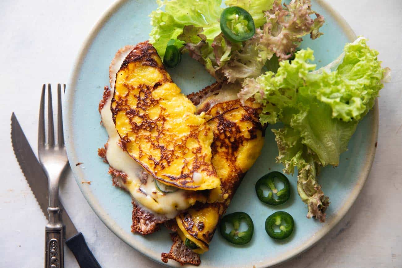 an image of cheese filled cachapa on a blue plate with sliced jalapeno and lettuce on the side