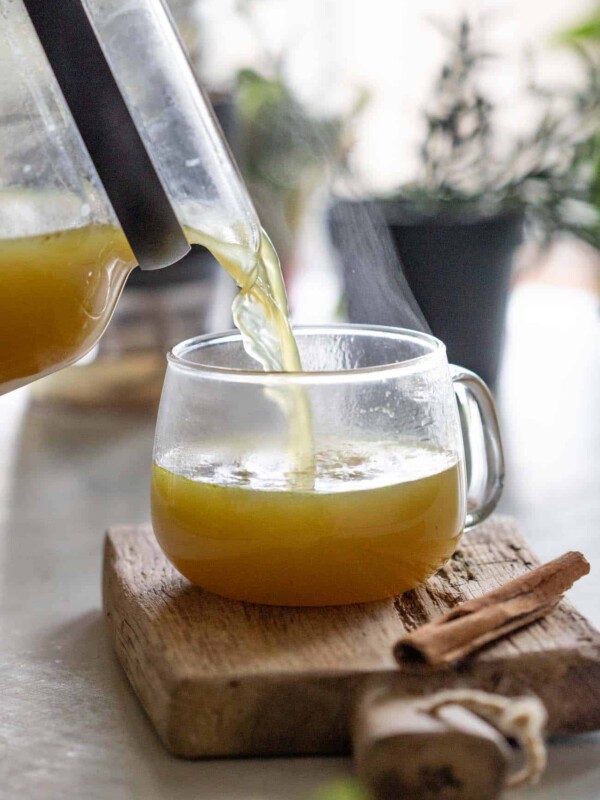 shot of turmeric chicken bone broth being poured into a clear glass mug resting on a wooden board