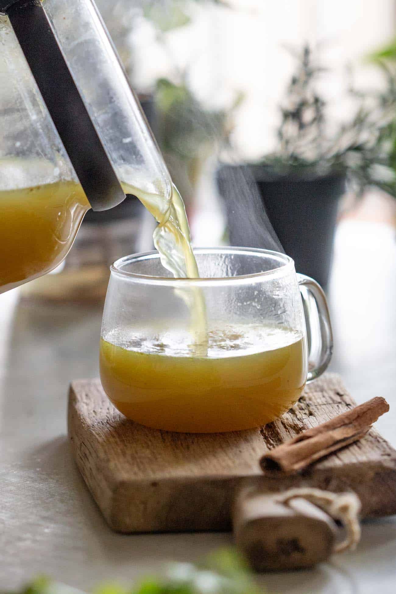 shot of turmeric chicken bone broth being poured into a clear glass mug resting on a wooden board