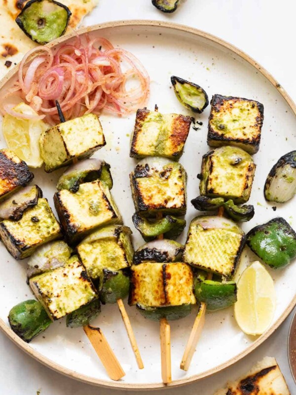 a shot of hariyali paneer tikka on skewers placed on a white plate