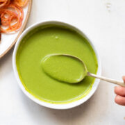 mint chutney served in a white bowl with a spoonful of chutney being taken out