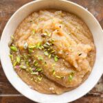 a white bowl with sooji halwa with sprinkled pistachio on top