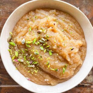 a white bowl with sooji halwa with sprinkled pistachio on top