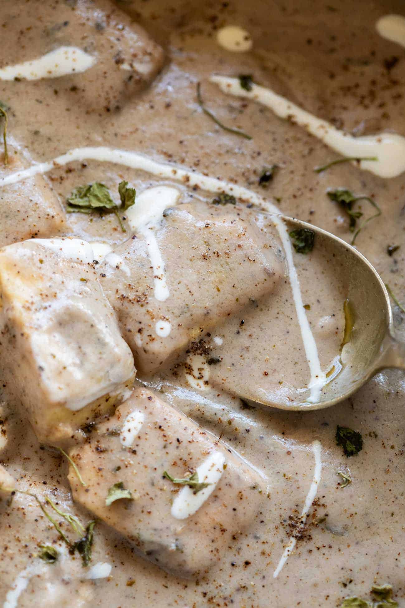 close up shot of paneer kali mirch gravy served in a bowl with cream drizzled on top