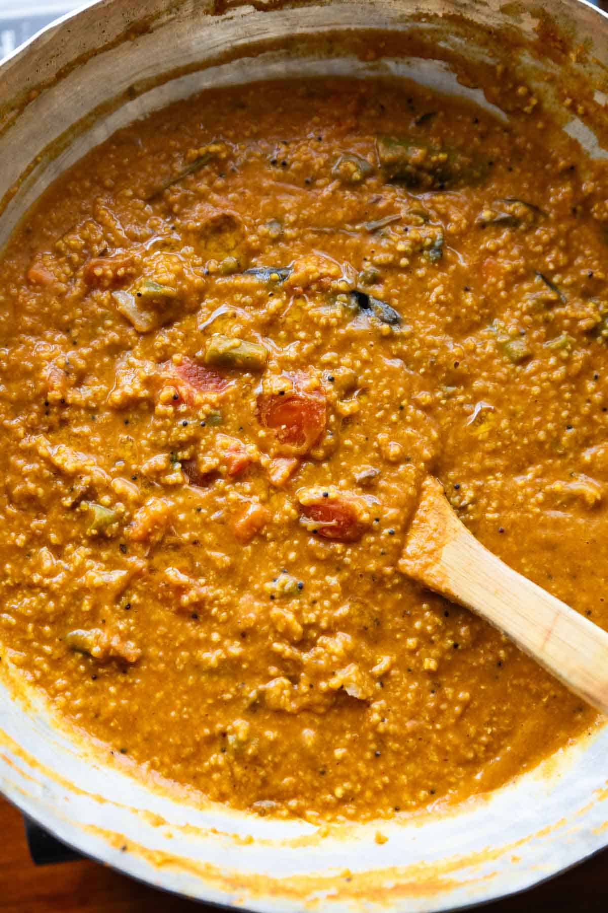 Millet bisi bele bath in a kadai with a wooden spoon