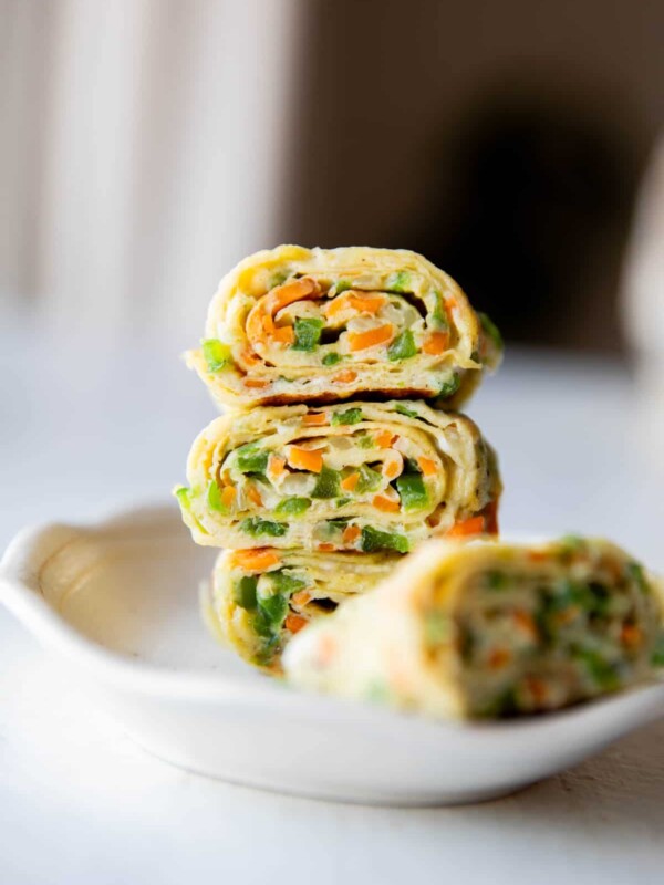 a close up shot of korean omelette roll stacked one on top of the other in a white bowl
