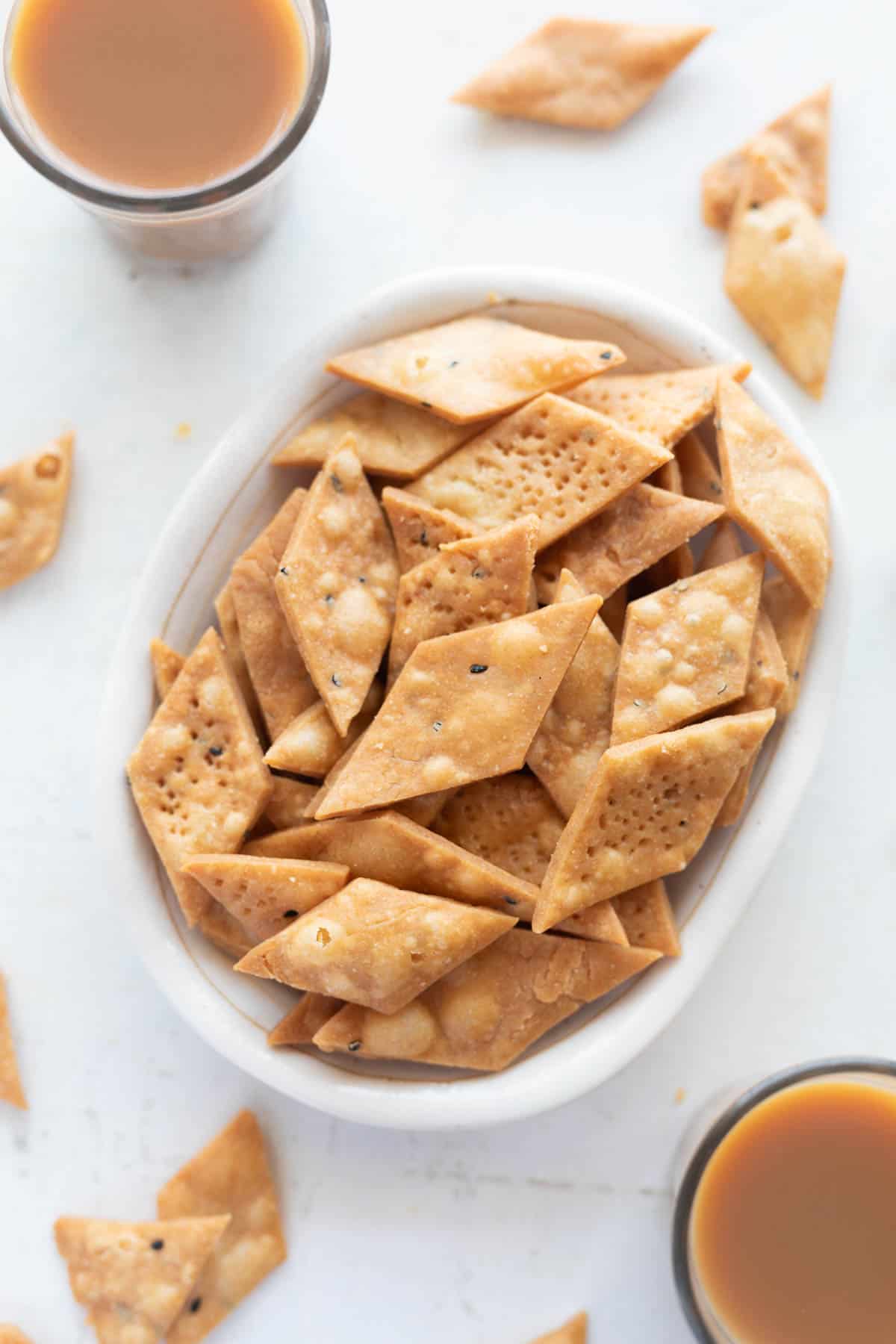 Picture of namak para in a white bowl with cups of chai around it