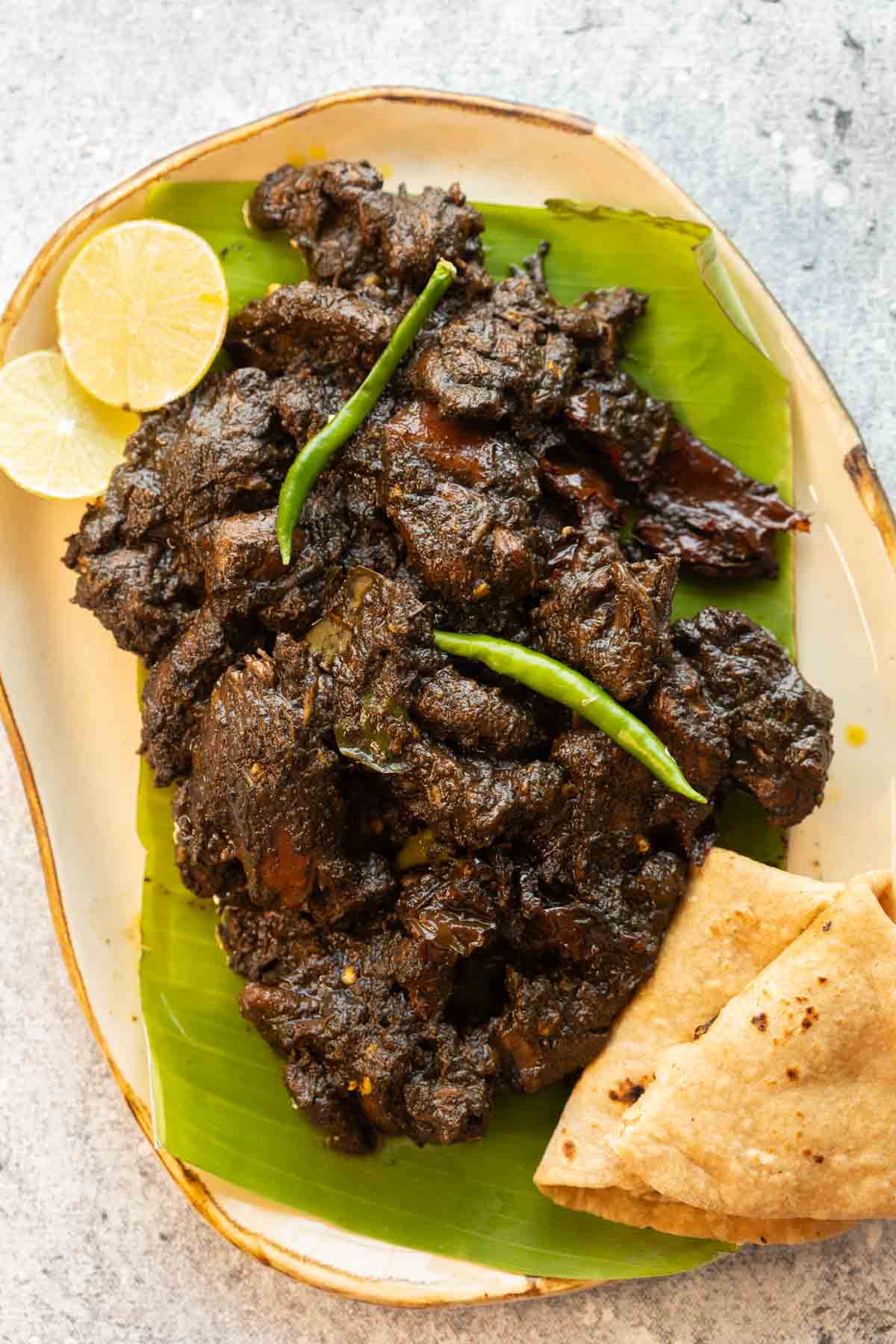 Black sesame chicken served on a platter with rotis and lime