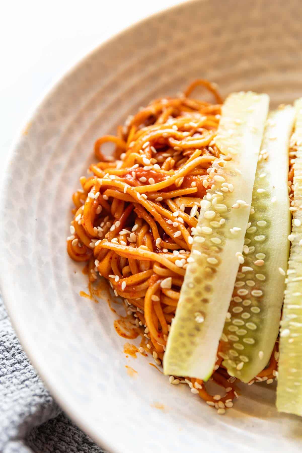 bibim guksu garnished with cucumber in a white bowl