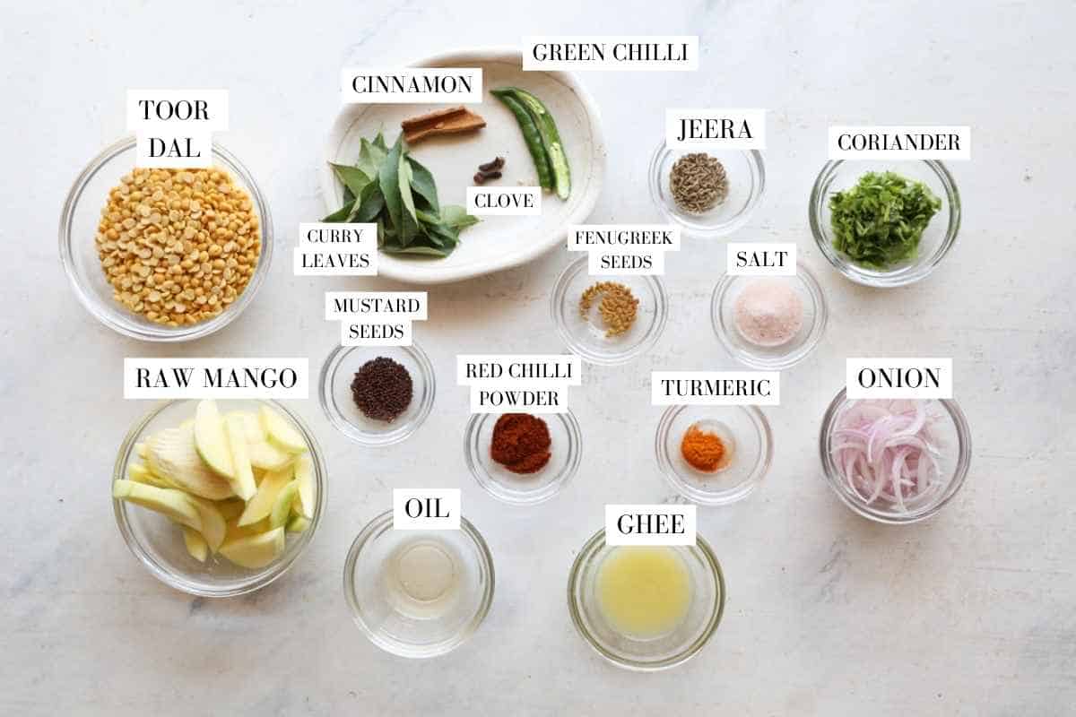 raw mango dal ingredients placed in transparent bowls on a white surface