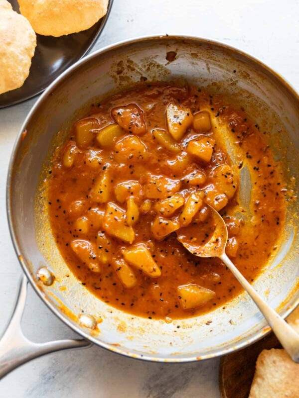 Raw mango chutney in a pan with a spoon and served with pooris