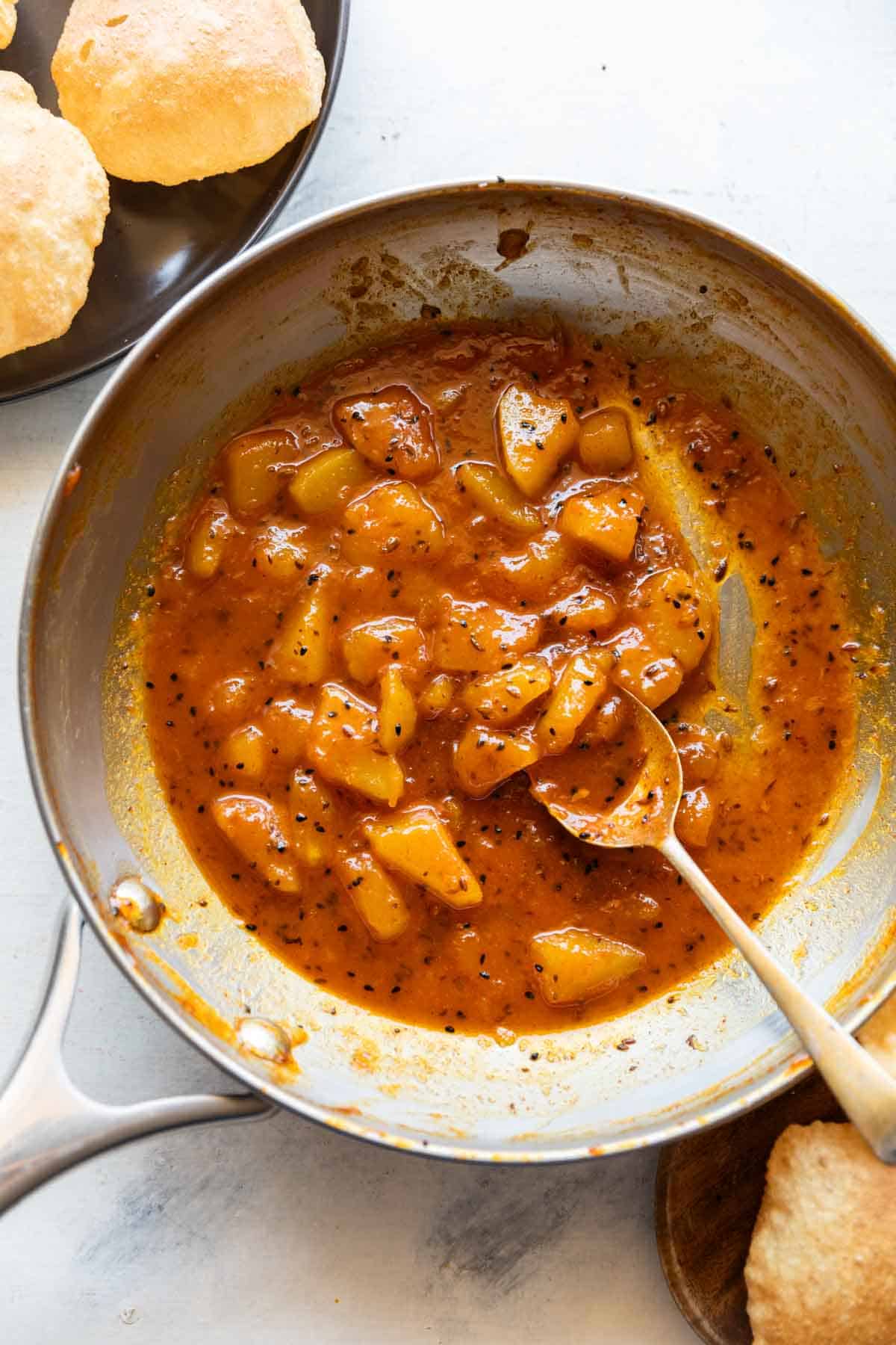 Raw mango chutney in a pan with a spoon and served with pooris